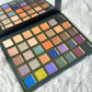 A large eyeshadow palette with multiple square pans of colorful makeup, shown open on a white faux-fur surface. The palette has shades including beige, orange, brown, green, blue, purple, and pink, with a mirror visible inside the upper section.
