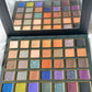 A 35-shade eyeshadow palette with a built-in mirror, shown open to display the various shades including oranges, purples, blues, greens, and sparkles, set against a white textured background.